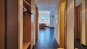 Un pasillo con puertas de madera, un perchero y vista hacia un comedor con una mesa y sillas.