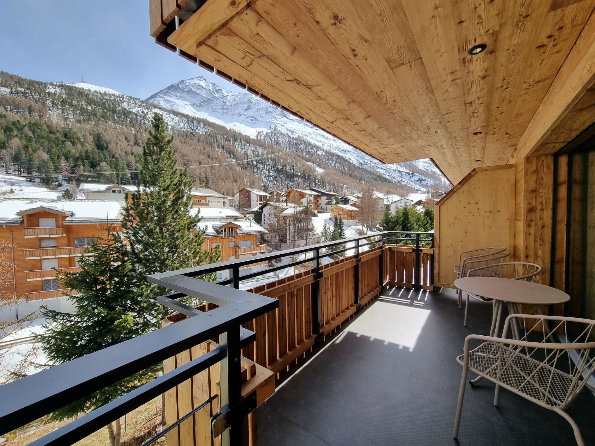 A wooden balcony with a view of snow-covered mountains and a town below.
