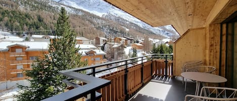 A wooden balcony with a view of snow-covered mountains and a town below.