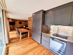 Uma cozinha moderna com armários cinza, uma mesa de jantar de madeira e um forno embutido.