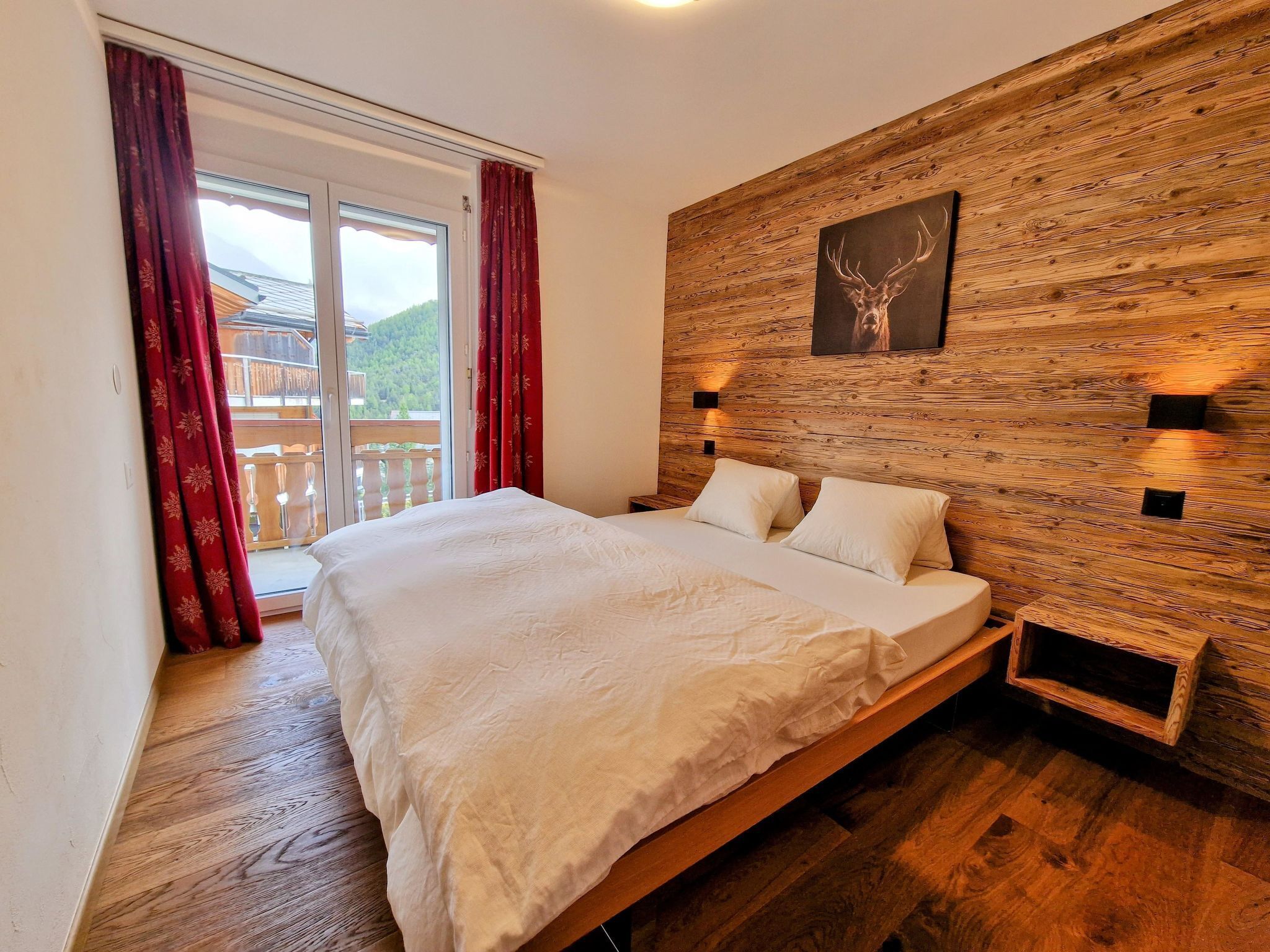 Ein Schlafzimmer mit einem großen Bett, Holzvertäfelung, einem Wandbild und einem Balkon mit roten Vorhängen.