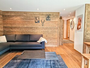 A modern living room with a dark grey sectional sofa, a small coffee table, and a wooden accent wall. - Cornelia 1 Appartement/Fewo Appartement/Fewo by Interhome (Saas-Fee)