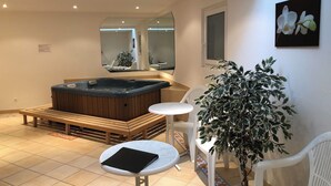 Ein modernes Badezimmer mit einer Holzbank, einem kleinen runden Tisch, einer Topfpflanze und einem großen Spiegel.