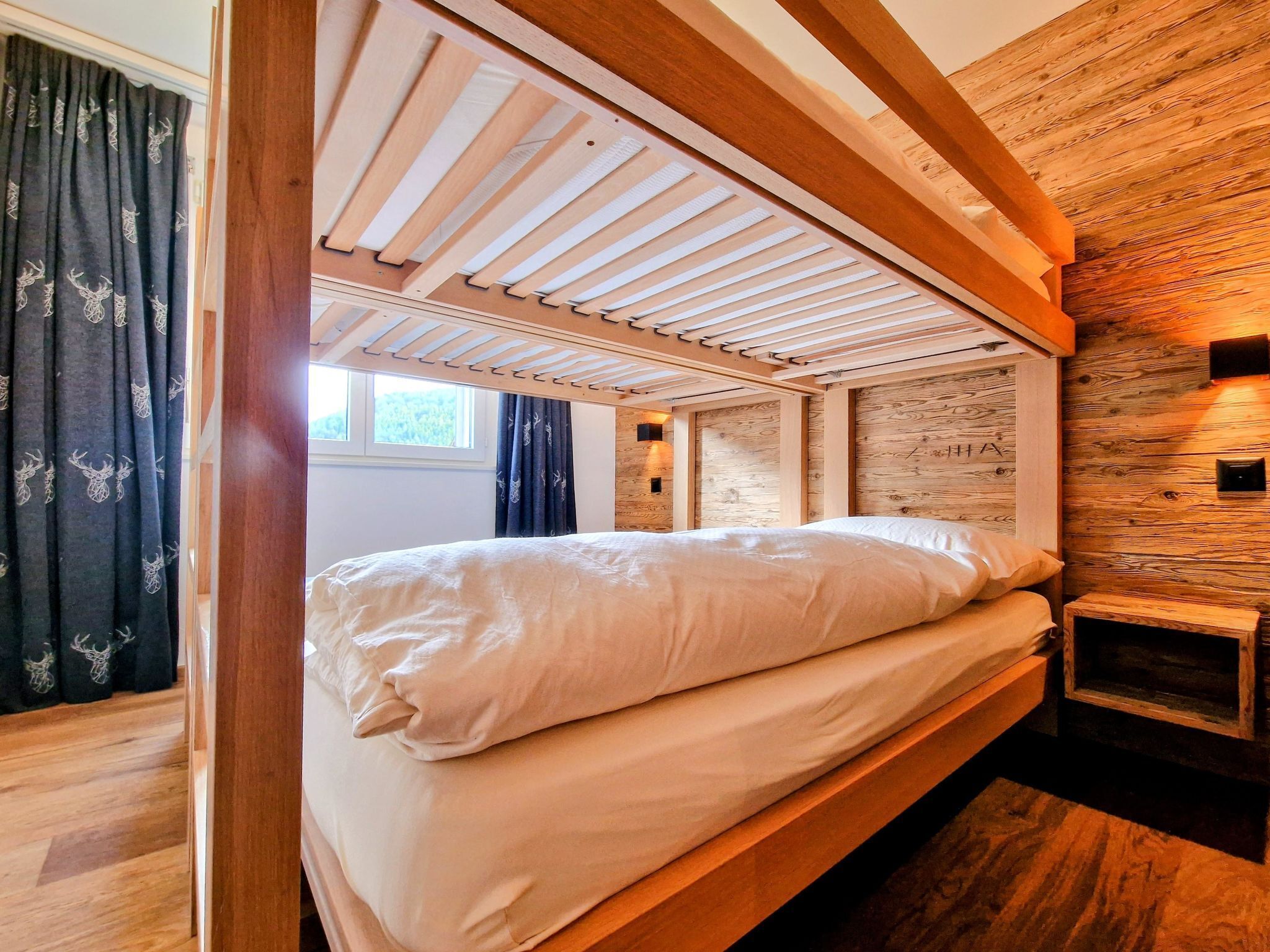 A bunk bed with a wooden headboard and slatted ceiling, a small bedside table, and a wall with a wooden panel design.