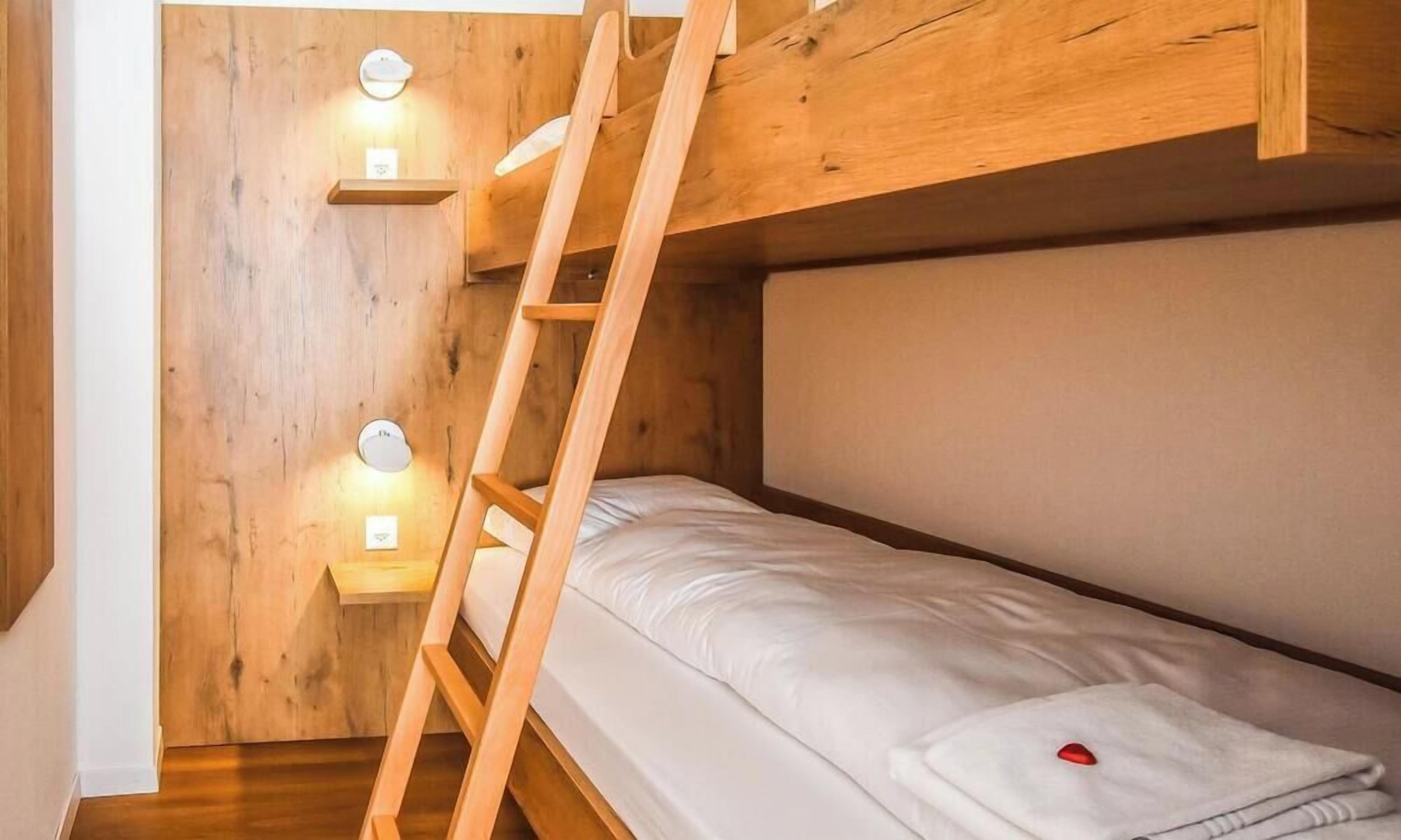 A bunk bed with a wooden ladder, a small shelf, and two wall-mounted lights.