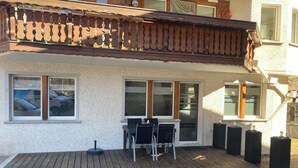 Un edificio con terraza de madera, mesa y sillas, y amplios ventanales.