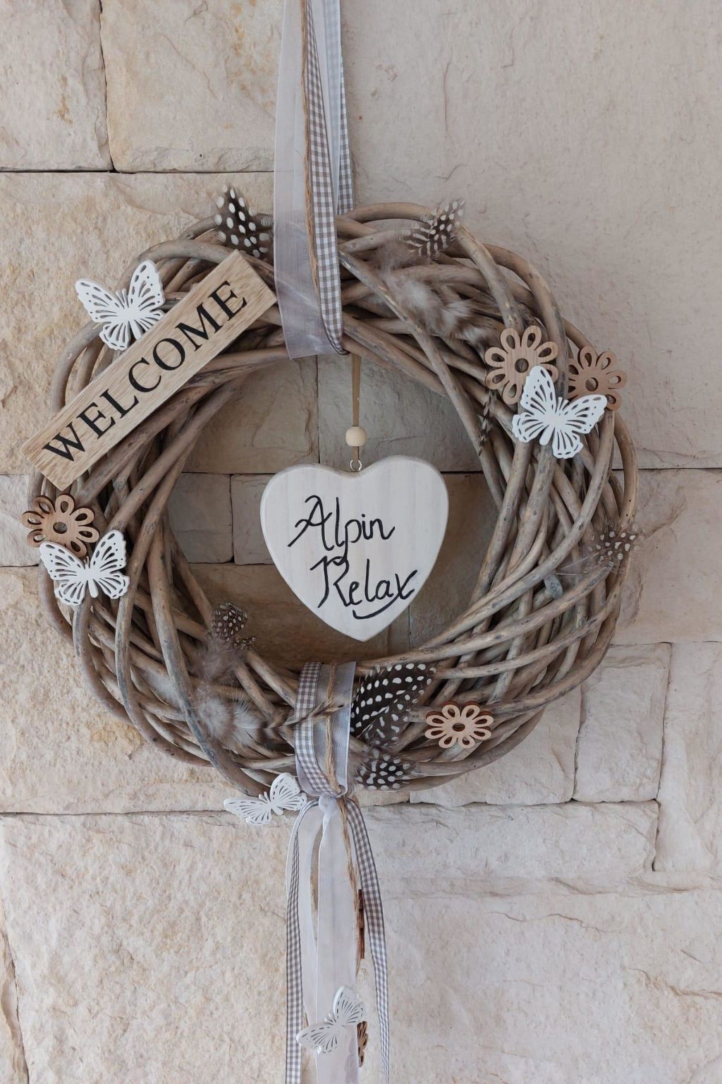 Una corona decorativa amb un cartell amb forma de cor que diu 'Alpin Relax' i un cartell de 'WELCOME' a una paret de pedra.