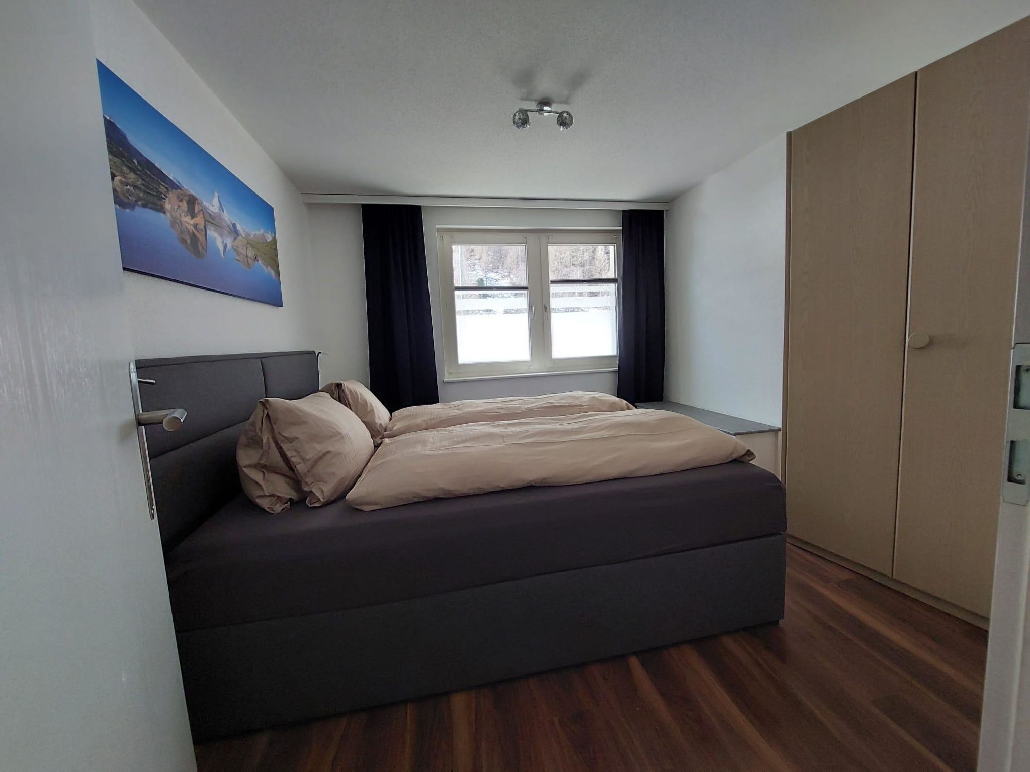 Un dormitorio con cama, ventana con cortinas, un cuadro en la pared y un armario.