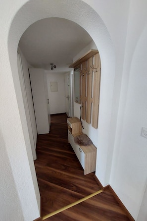 Um corredor com piso de madeira, parede branca e um armário de madeira com espelho.