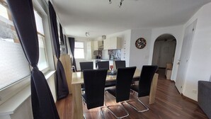 Un comedor moderno con una mesa de madera y sillas negras, una cocina al fondo y un pasillo que conduce a otra habitación.