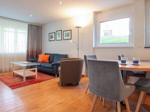 A modern living room with a sofa, armchair, coffee table, and a dining area with chairs and a table. - Dolce Vita Appartement/Fewo 2-Bettwohnung Allalin by Interhome (Saas-Fee)
