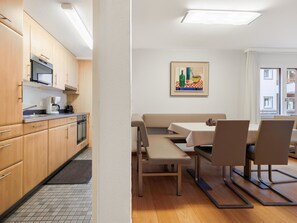 Eine moderne Küche mit Holdekor, einer Mikrowelle und einer Kaffeemaschine. Ein Essbereich mit Tisch und Stühlen lädt zum Verweilen ein, und ein Gemälde ziert die Wand.