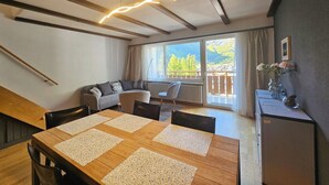 Un salon moderne avec une table à manger en bois, un canapé et une vue sur les montagnes grâce à de grandes fenêtres.