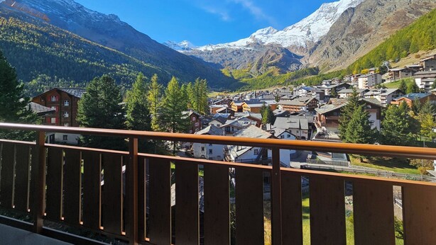Une ville de montagne entourée de sommets enneigés, d’une forêt dense et dotée de différents types de bâtiments.