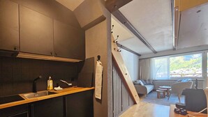 Une cuisine moderne avec des meubles de couleur sombre, un plan de travail en bois et un évier. Un escalier mène à un balcon aménagé avec des sièges d’extérieur.