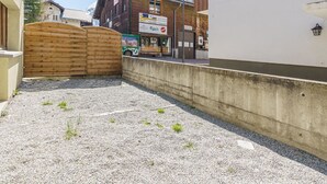 A gravel courtyard with a wooden gate, a building with a sign for a transport service, and a mountain backdrop. - Haus Slalom Appartement/Fewo Apt #1 by Interhome (Saas-Fee)