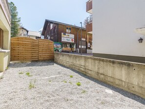 A gravel courtyard with a wooden gate, a building with a sign for a transport service, and a mountain backdrop. - Haus Slalom Appartement/Fewo Apt #1 by Interhome (Saas-Fee)