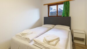 A single bed with white linens and towels, a small bedside table, and a window with a view of a snowy landscape. - Haus Slalom Appartement/Fewo Apt #1 by Interhome (Saas-Fee)