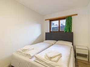 A single bed with white linens and towels, a small bedside table, and a window with a view of a snowy landscape. - Haus Slalom Appartement/Fewo Apt #1 by Interhome (Saas-Fee)