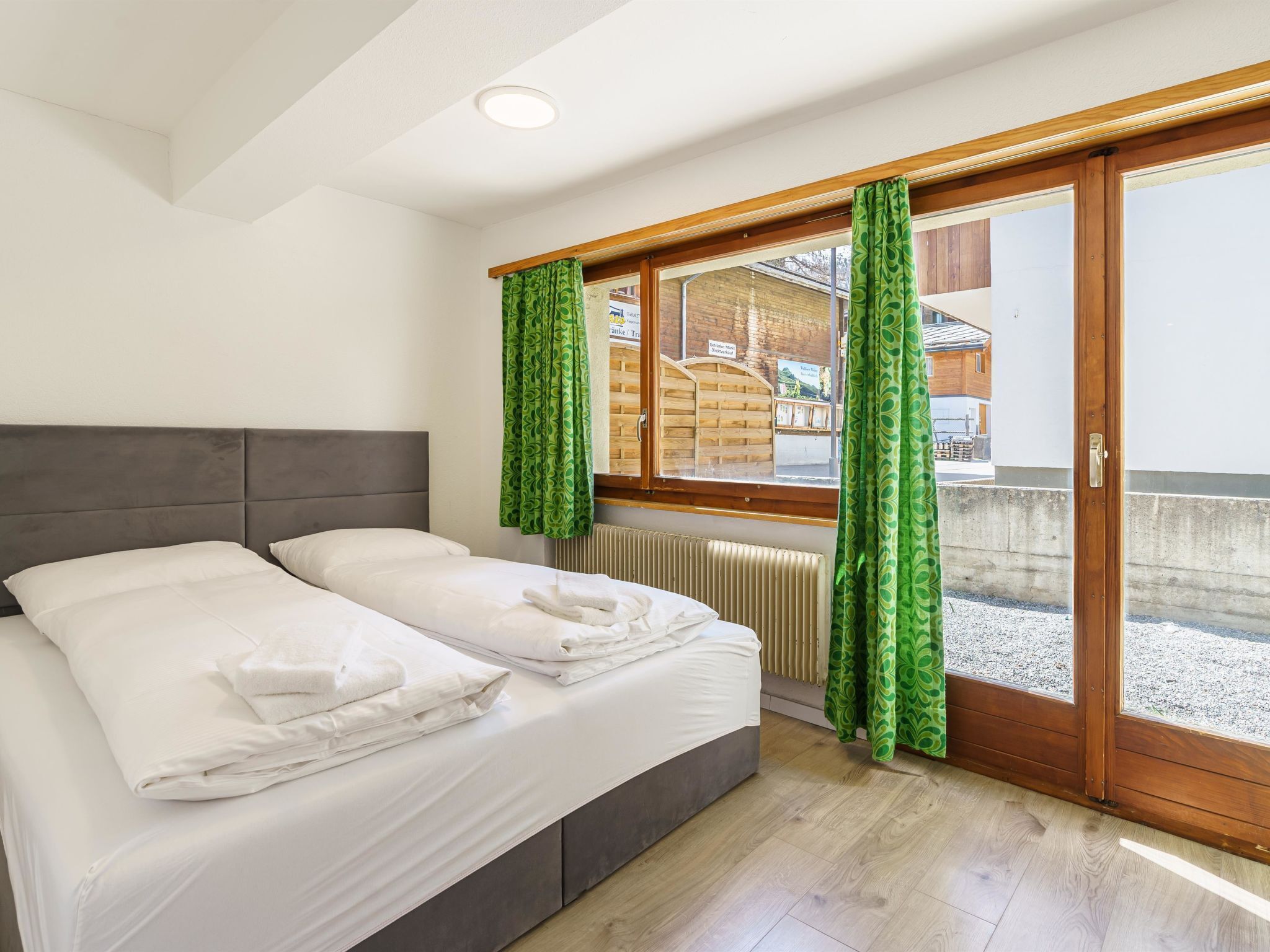 Ein Schlafzimmer mit einem Doppelbett, einem Heizkörper und einem Fenster mit grünen Vorhängen.