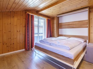 Une chambre à coucher aux murs lambrissés, avec un lit, des rideaux et une fenêtre.