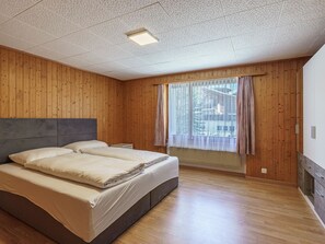 A bedroom with a large bed, wooden walls, a window with curtains, and a ceiling with a grid pattern. - Haus Slalom Appartement/Fewo Apt #2 by Interhome (Saas-Fee)
