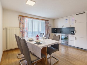 A compact kitchen with a dining area, including a table set for four, chairs, and a radiator. - Haus Slalom Appartement/Fewo Apt #2 by Interhome (Saas-Fee)