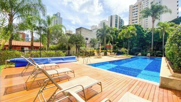 Una piscina con sillones de descanso, rodeada de vegetación y edificios altos.