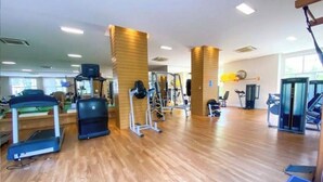 Un gimnasio con cintas de correr, máquinas de pesas y piso de madera.