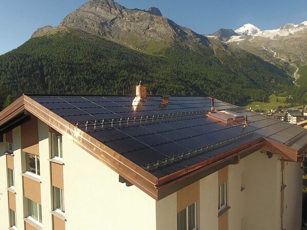 Een gebouw met een dakbedekt met zonnepanelen, een schoorsteen en een bergachtige achtergrond.