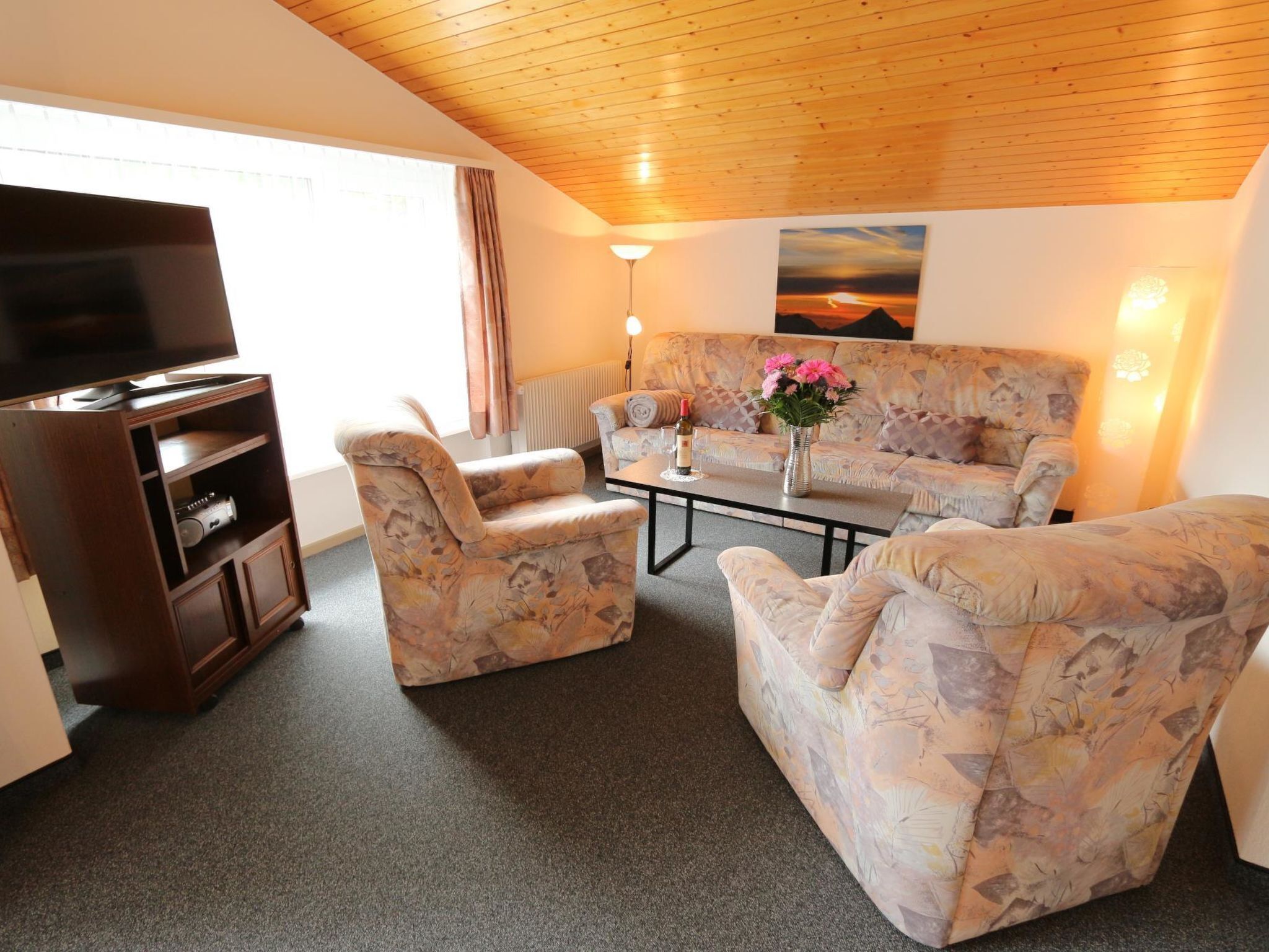 A living room with a sofa, two armchairs, a coffee table, a TV, and a lamp.