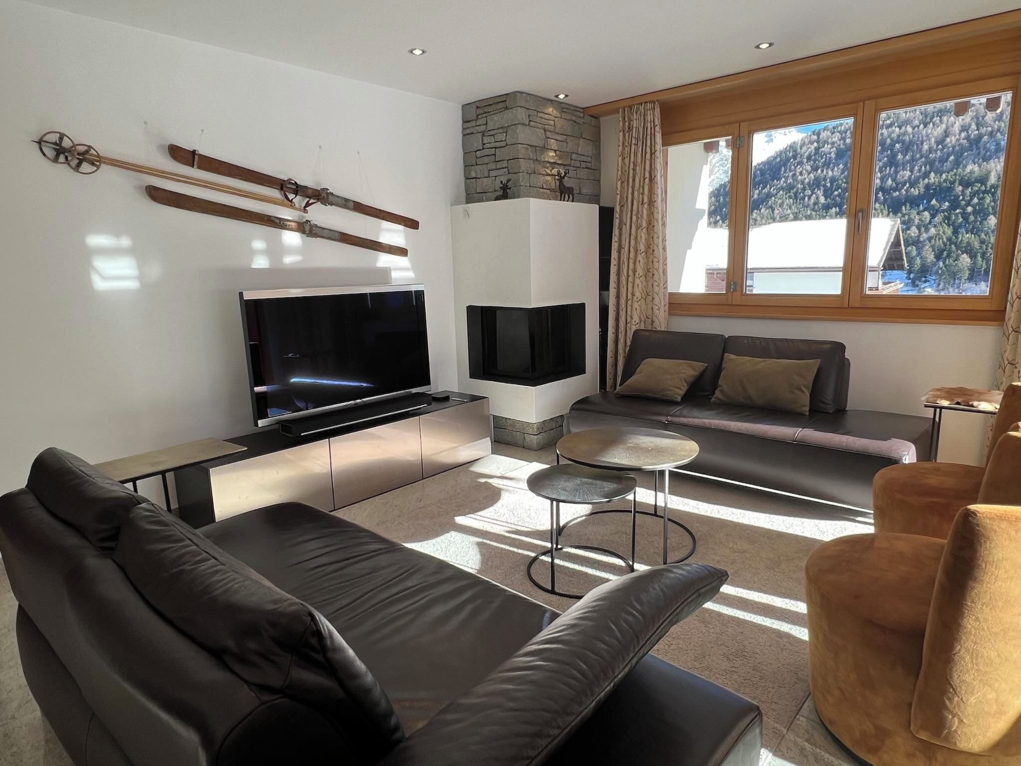 A modern living room with a flat-screen TV, a stone fireplace, a sofa, and a view of a snowy landscape through a window.