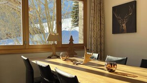 Ein Essbereich mit einem Holztisch, Stühlen, einer Lampe, einer Glaskugel, einem kleinen Weihnachtsbaum und einem Bild eines Hirschkopfes an der Wand.