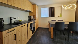 A modern kitchen with wooden cabinets, a black countertop, and a dining area with a table and chairs. - Haus Rio EG Appartement/Fewo Appartement/Fewo by Interhome (Saas-Fee)