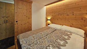 A bedroom with a wooden headboard, a bed with patterned bedding, and a wardrobe with a wooden finish. - Haus Rio EG Appartement/Fewo Appartement/Fewo by Interhome (Saas-Fee)