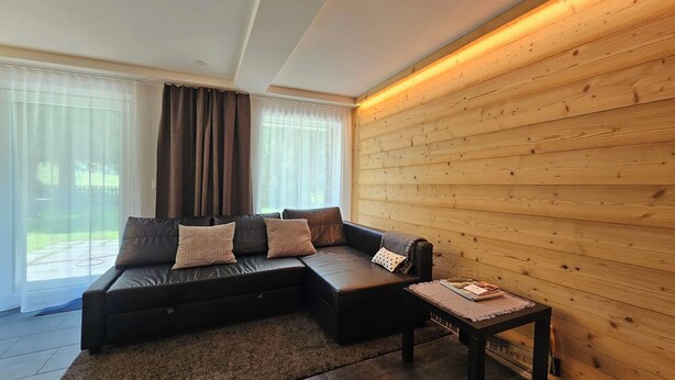 A modern living room with a sectional sofa, a small table, and a wooden accent wall. - Haus Rio EG Appartement/Fewo Appartement/Fewo by Interhome (Saas-Fee)