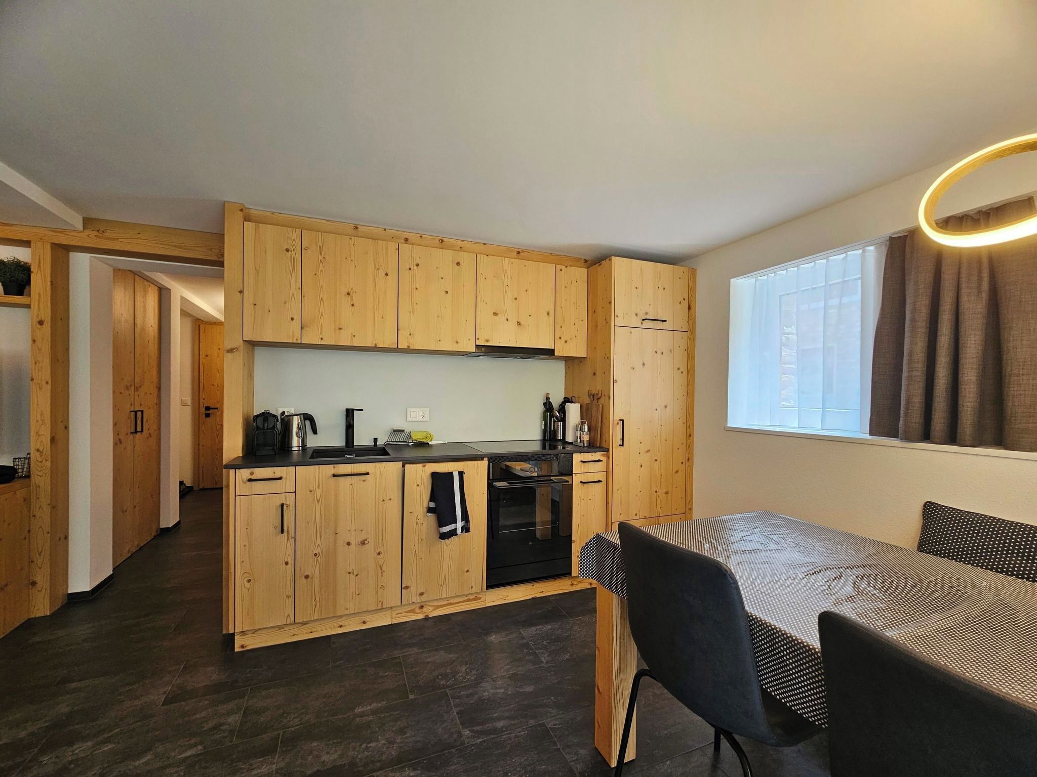 A compact kitchen with wooden cabinets, a black countertop, and a dining area with a table and chairs.