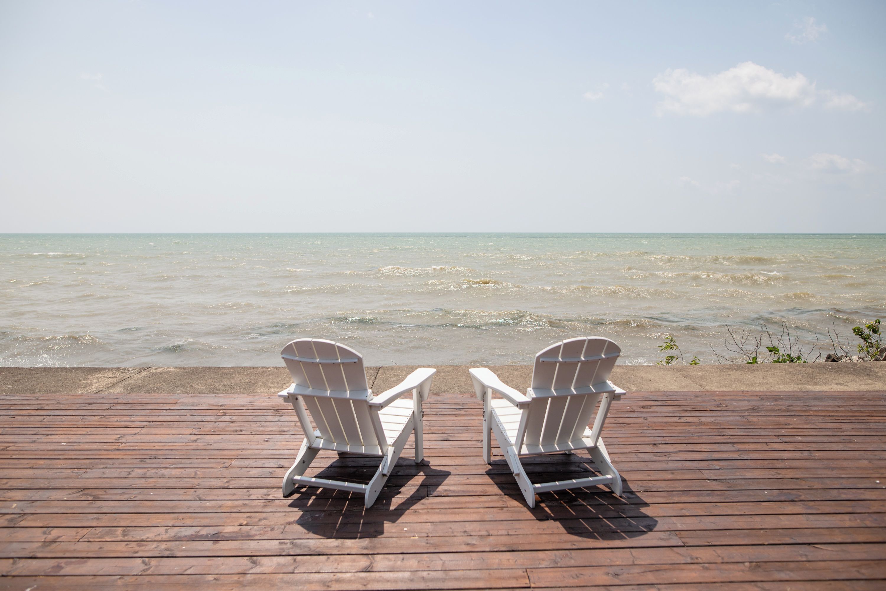 Deux chaises Adirondack blanches, placées face à une plage et à une terrasse en bois.