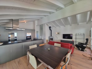 Eine moderne Küche mit einer zentralen Kochinsel, einem Essbereich mit dunklem Holztisch und einem roten Sofa im Wohnbereich.
