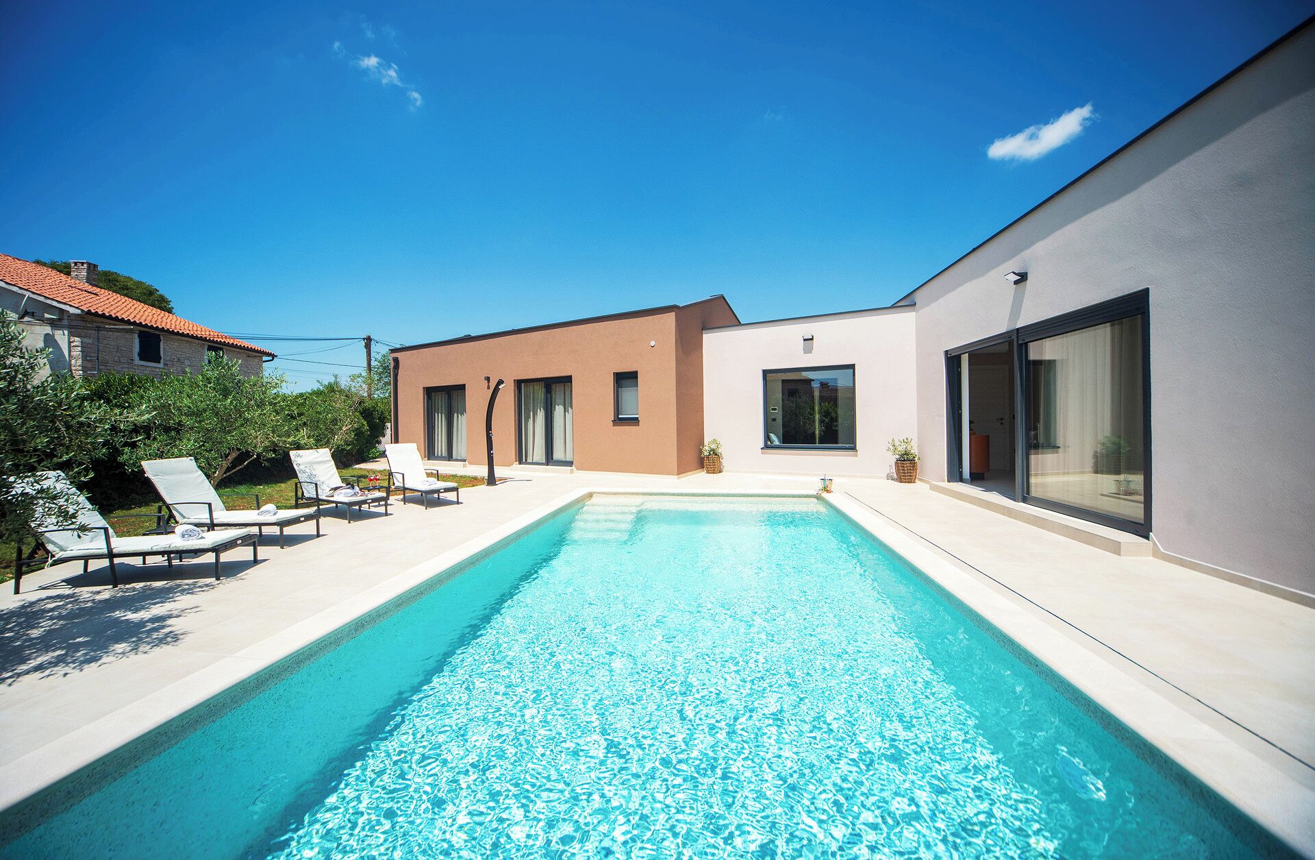 A modern pool area with a clear blue pool, sun loungers, and a building with large windows.