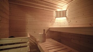 A wooden sauna with benches, a bucket, and a wall-mounted light. - Chalet Wilhelmina Appartement/Fewo, Dusche und Bad, WC, 8-Bettwohnung by Interhome (Arosa)