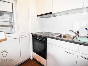 Eine moderne Küche mit weißen Schränken, einem Geschirrspüler, einem Backofen und einer Spüle aus Edelstahl.