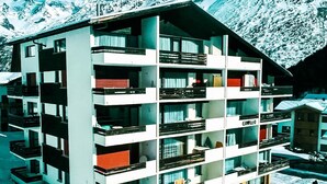 A multi-story hotel with balconies, a ski slope in the background, and a mountainous landscape. - Haus Camillo Appartement/Fewo 4-Bettwohnung Nr. 16 by Interhome (Saas-Fee)