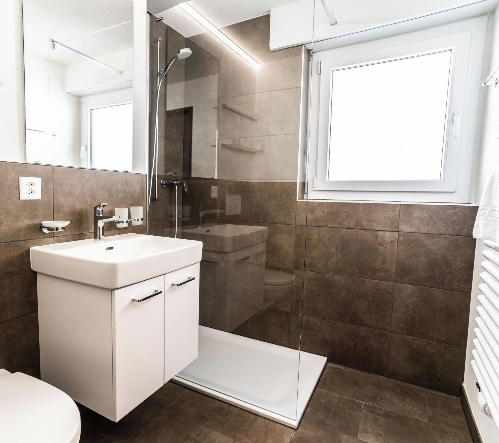A modern bathroom with a white sink, a glass shower enclosure, and a window.