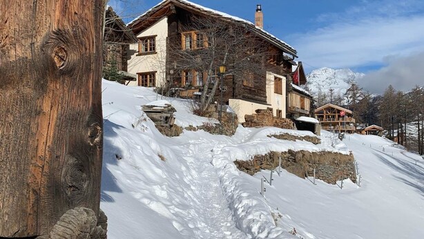 Eine Holzhütte mit Steinfundament, verschneitem Dach und freiem Blick auf die umliegenden Berge.
