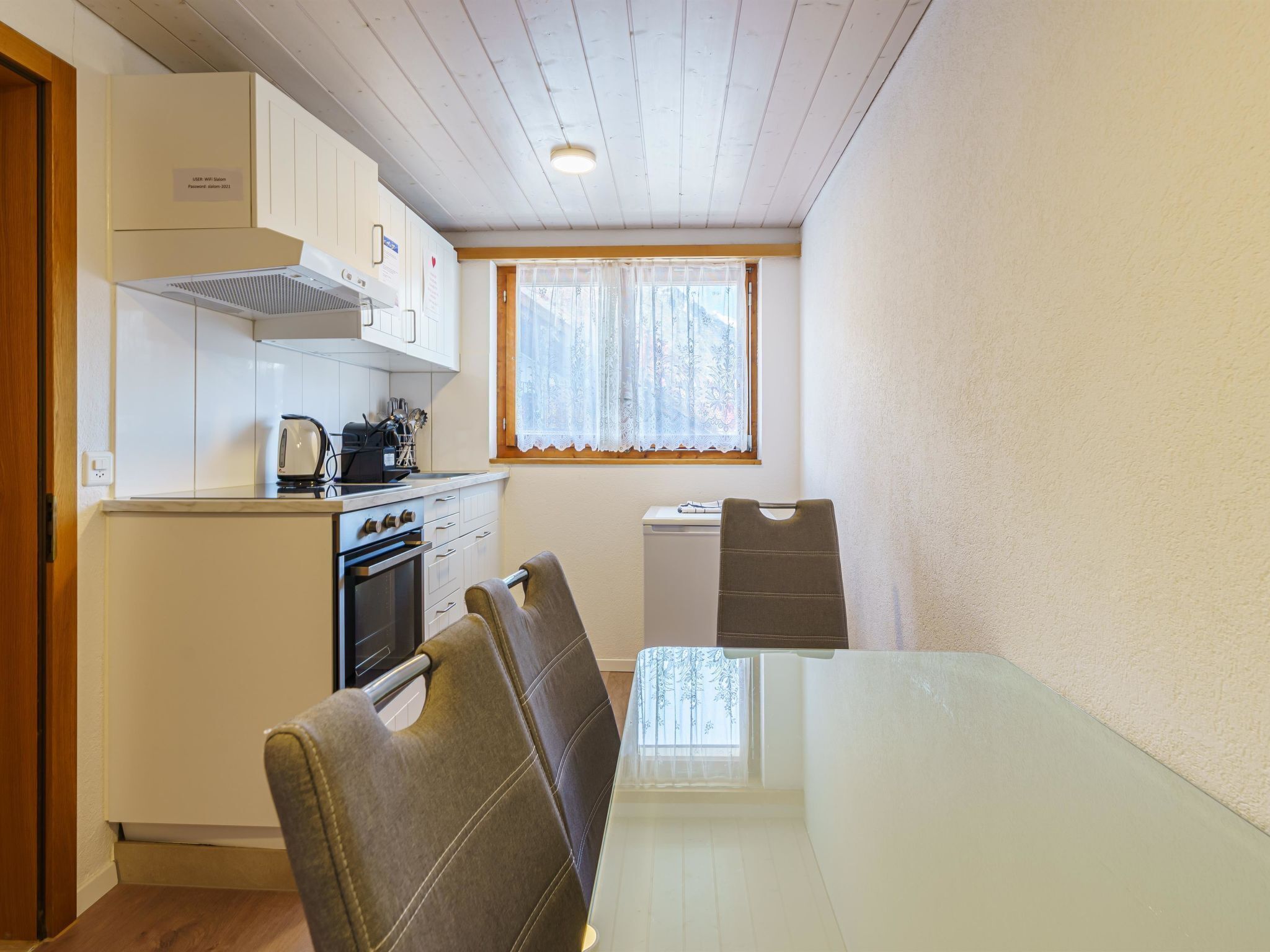 Una cocina compacta con estufa, horno y ventana con cortinas. Hay una mesa de comedor con sillas.