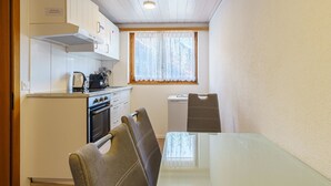 A compact kitchen with a stove, oven, and a window with curtains. There is a dining table with chairs. - Haus Slalom Appartement/Fewo Apt #7 by Interhome (Saas-Fee)