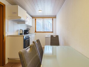 A compact kitchen with a stove, oven, and a window with curtains. There is a dining table with chairs. - Haus Slalom Appartement/Fewo Apt #7 by Interhome (Saas-Fee)