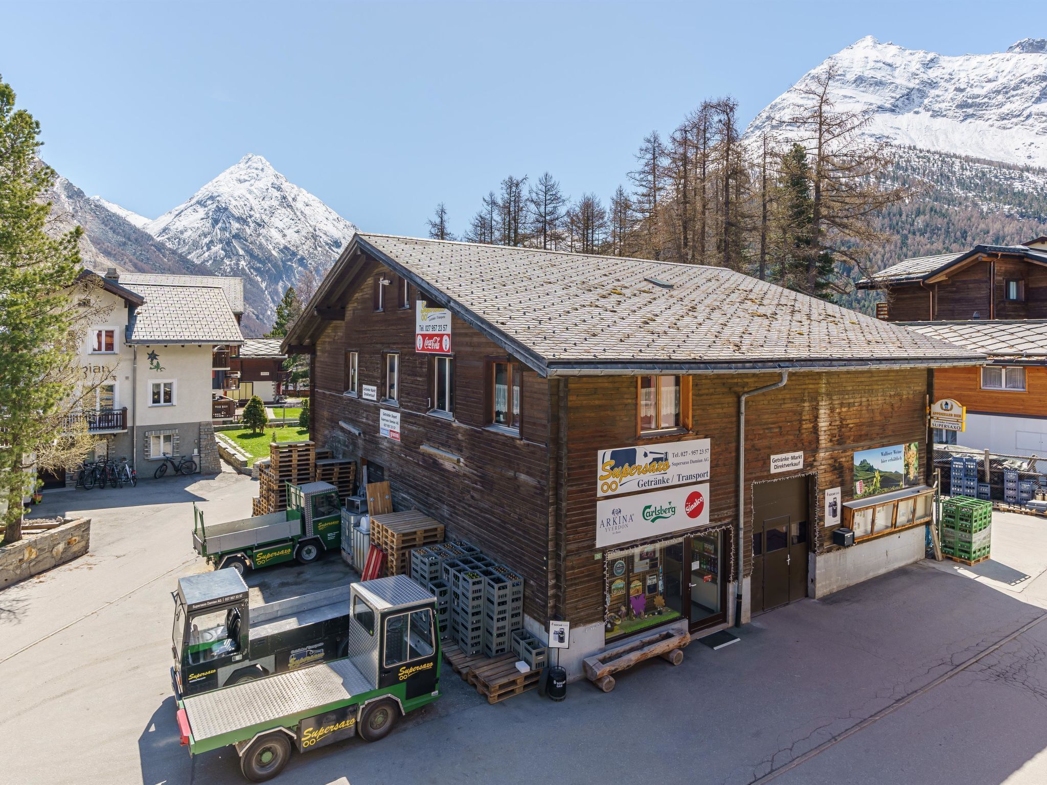 A mountain town with a wooden building featuring a Coca-Cola sign, surrounded by snow-capped mountains.