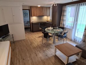 Ein modernes Wohnzimmer mit einem Glastisch, schwarzen Stühlen, einem Couchtisch aus Holz und einem Fernseher auf einem Lowboard.